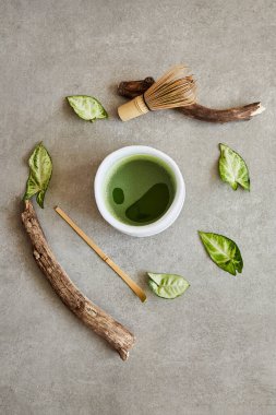 Organik yeşil kibrit çayı, çay aksesuarları, tahta çubuklar ve gri taş yüzeyde yapraklar..