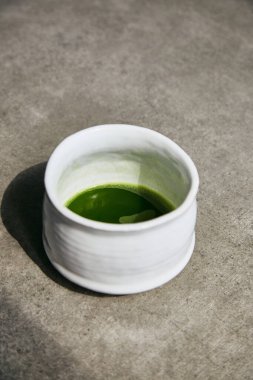 Gri yüzeydeki Chawan kasesinde organik yeşil kibrit çayı..