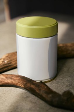 Kavanoz maketi. Yeşil kapaklı, gri bir yüzeye çay, kahve ve kuru tahta çubuklar depolamak için beyaz plastik bir kavanoz..