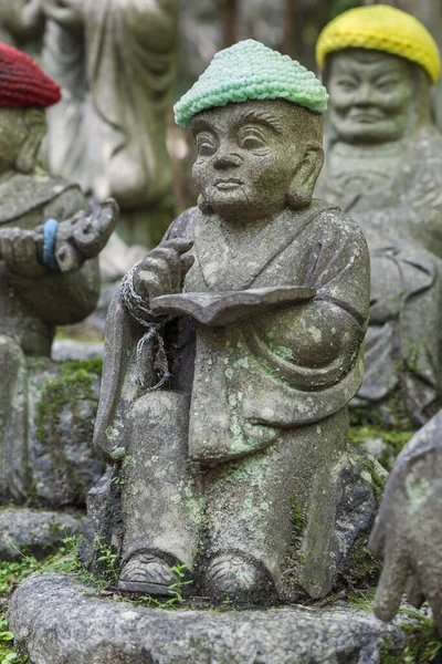 Stará kamenná socha buddhistického mnicha v pleteném klobouku s knihou v rukou. — Stock fotografie