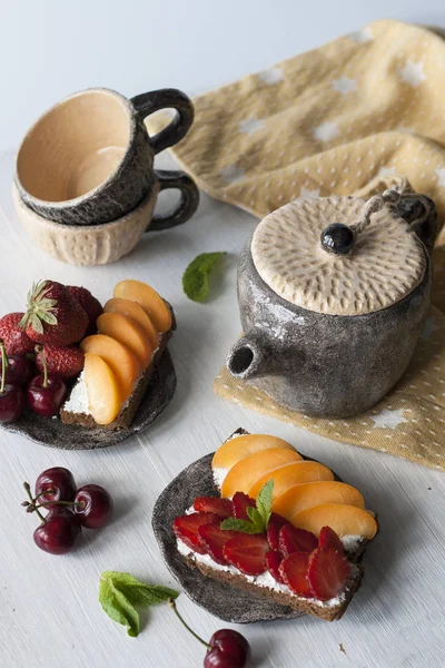 Sandwiches con queso dulce, frutas y bayas, y tazas de té — Foto de Stock