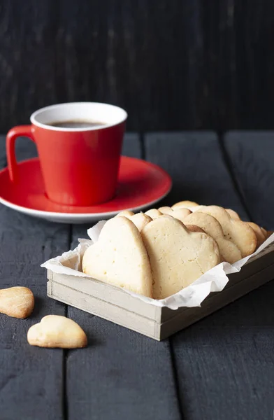 Red cup and cookie hearts on a black background — Stock Photo, Image