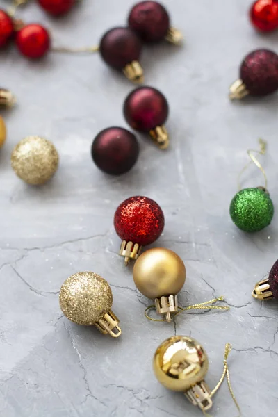 Leuchtend rote, kirsch-, grüne und goldene Weihnachtskugeln liegen auf einem grauen — Stockfoto