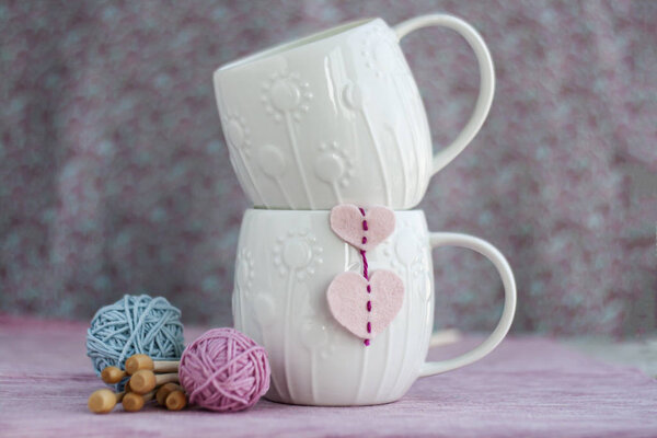 Two white cups stand one on one on a pink background, on one hea