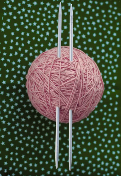 Ткань розовых ниток и вязаные иголки лежат на темно-зеленом — стоковое фото