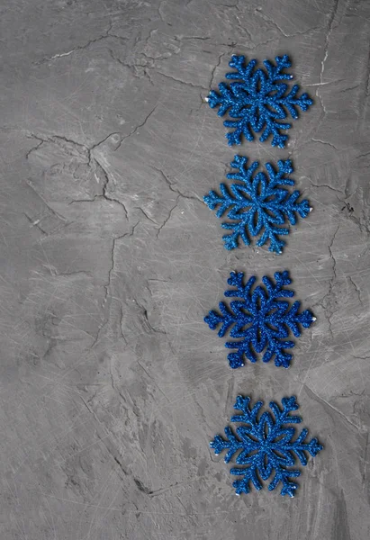 Muchos copos de nieve azules se encuentran en una fila sobre un fondo de hormigón gris . — Foto de Stock