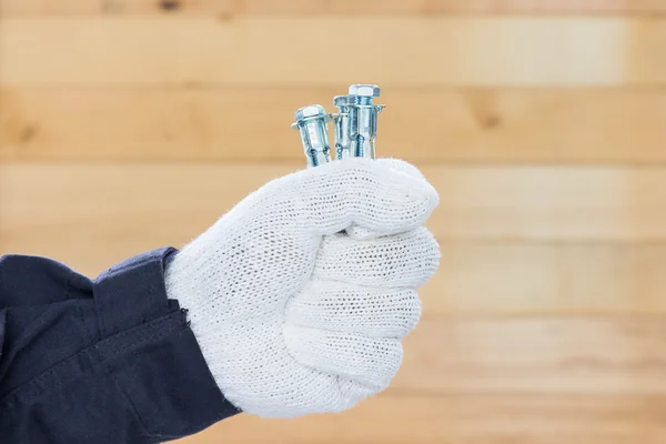 Dłoń w rękawicy trzyma śruby kotwiące metalowe — Zdjęcie stockowe