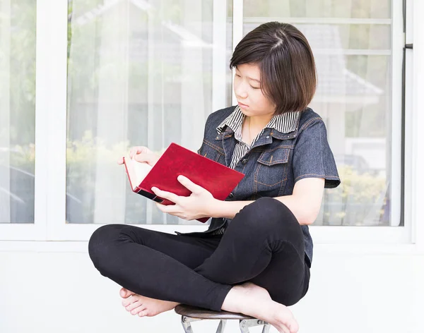 Młoda kobieta, czytanie książki, siedzi na krześle — Zdjęcie stockowe