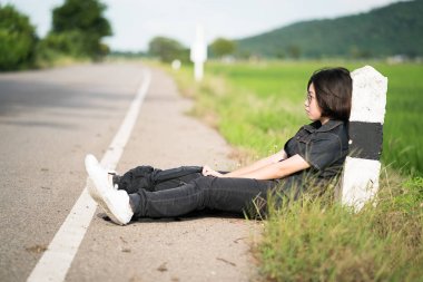 Kadın oturup kırsal bir yolda otostop sırt çantası ile