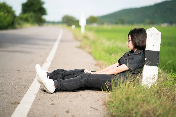 Kadın oturup kırsal bir yolda otostop sırt çantası ile