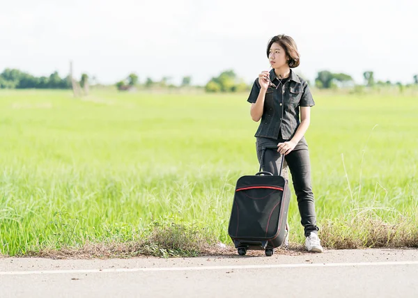 Woman with luggage hitchhiking along a road — Stock Photo, Image