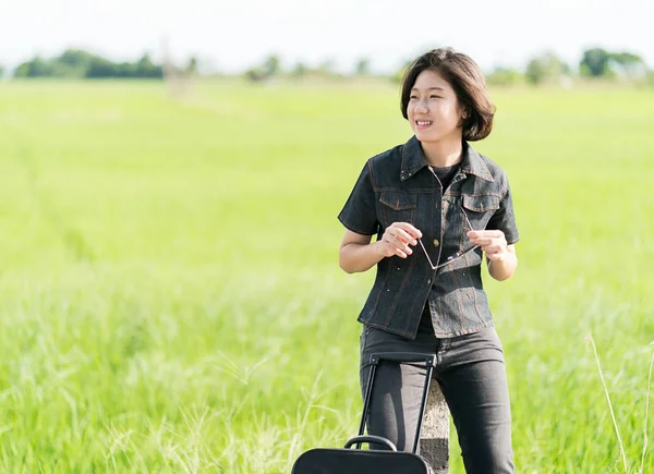 Woman with luggage hitchhiking along a road — Stock Photo, Image
