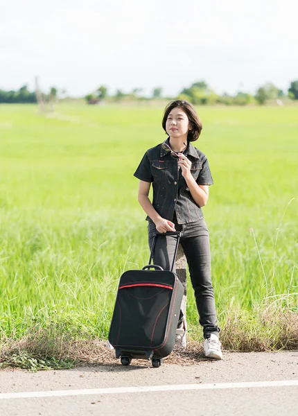 Mujer con equipaje haciendo autostop a lo largo de un camino —  Fotos de Stock