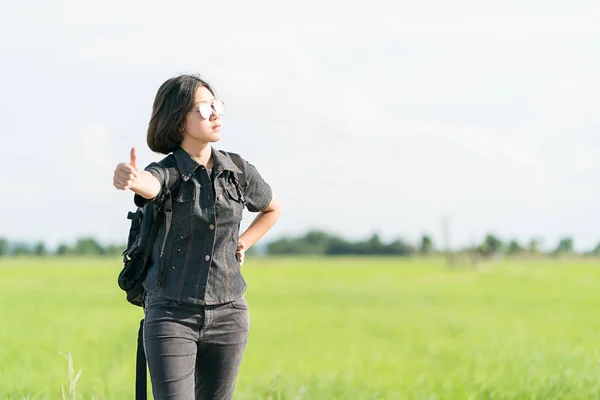 Woman with backpack hitchhiking along a road — Stock Photo, Image