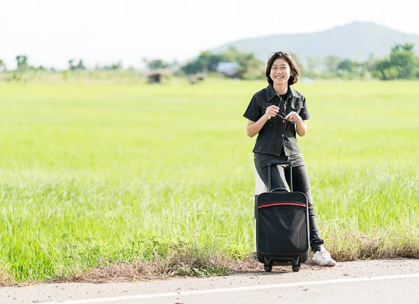 Woman with luggage hitchhiking along a road — Stock Photo, Image