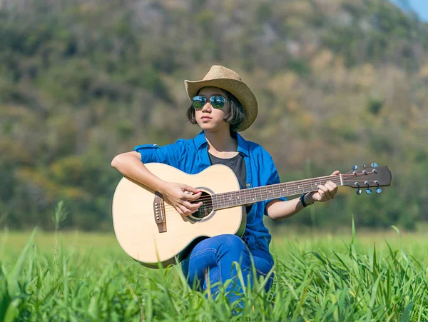 Kvinnor kort hår bära hatt och solglasögon sitter spela gitarr i g — Stockfoto