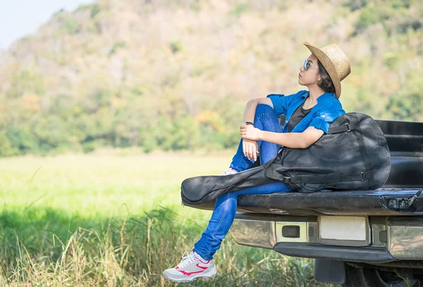 Woman wear hat and carry her guitar bag on pickup truck — Stock Photo, Image