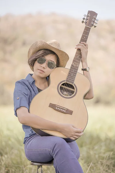 Kvinnor kort hår bära hatt och solglasögon sitter spela gitarr i g — Stockfoto