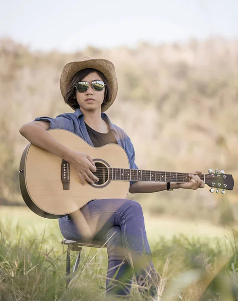 Kvinnor kort hår bära hatt och solglasögon sitter spela gitarr i g — Stockfoto