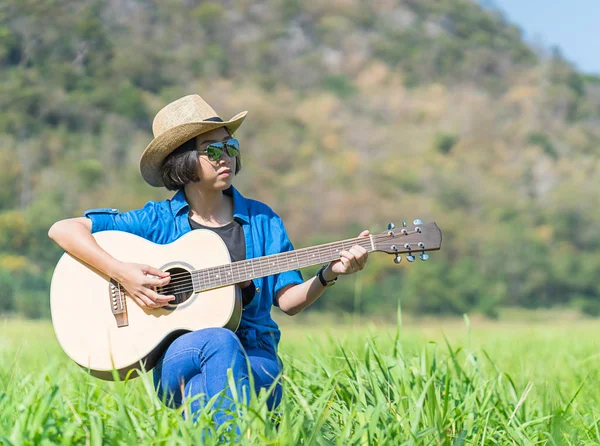 Frauen mit kurzen Haaren tragen Hut und Sonnenbrille sitzen und spielen Gitarre. — Stockfoto