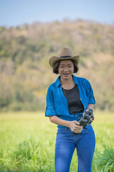 Жінка носить капелюх і тримає бінокль в трав'яному полі — стокове фото