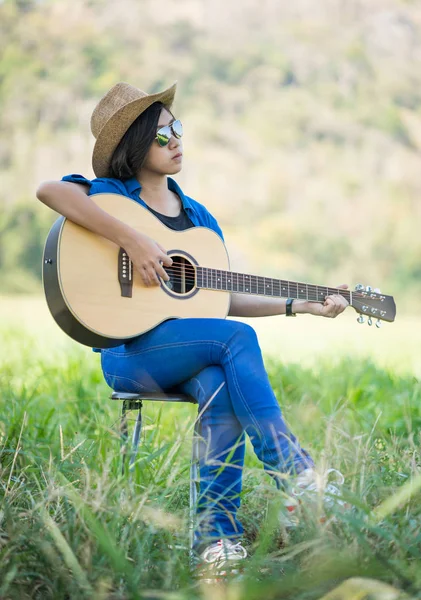 Frauen mit kurzen Haaren tragen Hut und Sonnenbrille sitzen und spielen Gitarre. — Stockfoto