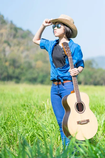 Kvinna bära hatten och bära sin gitarr i gräsplan — Stockfoto