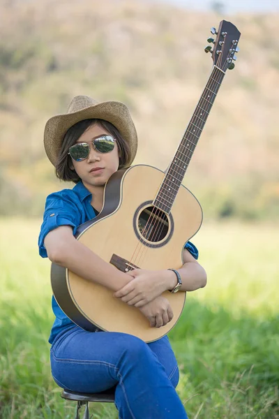 Kvinnor kort hår bära hatt och solglasögon sitter spela gitarr i g — Stockfoto