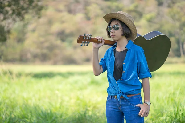 Kvinna bära hatten och bära sin gitarr i gräsplan — Stockfoto