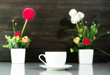 Kahve fincanı ve yapay çiçek vazosu masanın üzerinde.