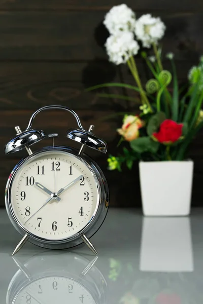 Relógio despertador e vaso de flores na mesa — Fotografia de Stock