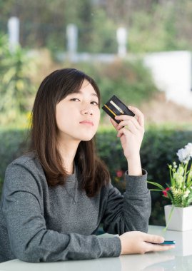 Genç bayan oturuyor ve kredi kartı gösteriyor. 