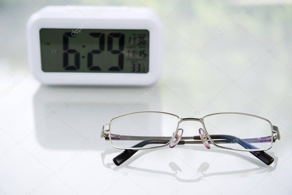 Eye glasses and Digital clock on table at home
