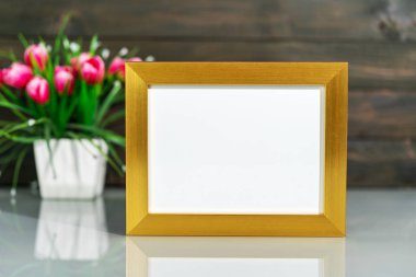 Resim, ahşap duvar zeminli masa üzerinde altın çerçeve ve yapay vazo buketi ile taklit