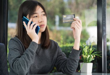 Kredi kartı tutan ve online alışveriş için akıllı telefon kullanan genç bir kadın.