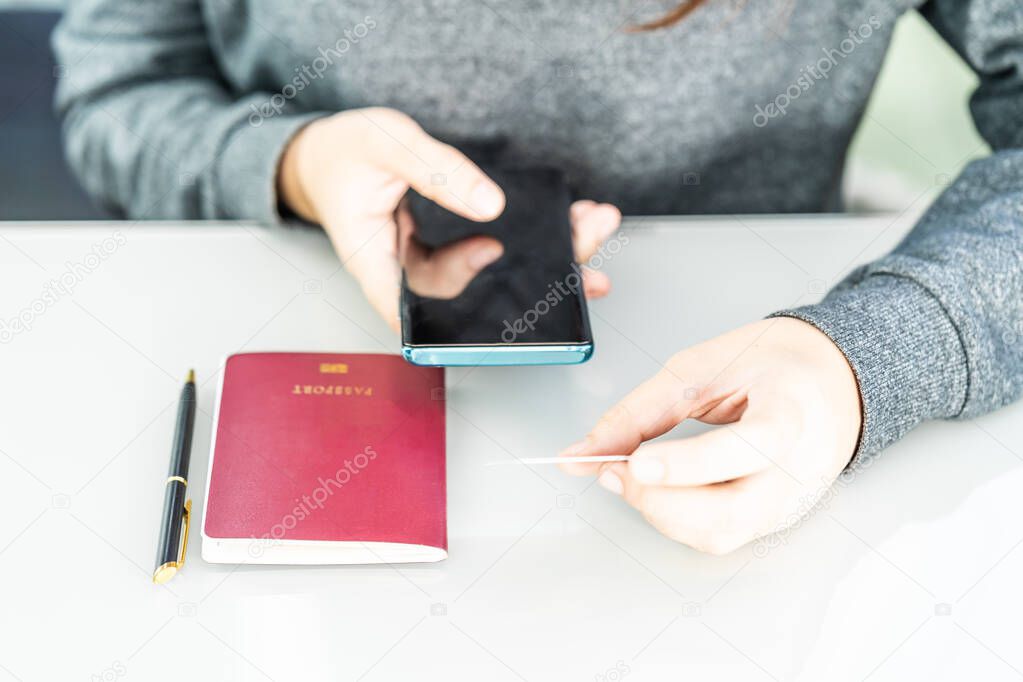 Woman holding credit card and passport using smartphone for online shoppingon deck in home office,Online shopping concept
