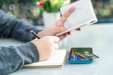 Not defterine kredi kartı ve akıllı telefon masasıyla yazı yazan kadının yakın plan resmi