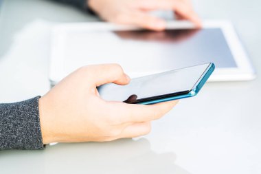 Elinde akıllı telefon tutan kadın dijital tablet üzerinde çalışıyor.