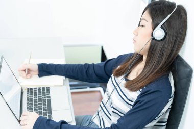 Genç bayan uzun saç oturma odasında oturuyor ve masa başında dizüstü bilgisayar kullanarak öğreniyor. E-öğrenme konsepti.