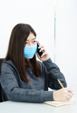 Uzun saçlı, koruyucu maske takan ve cep telefonu kullanan kadını kapat.