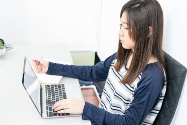 Genç bayan uzun saç oturma odasında oturuyor ve masa başında dizüstü bilgisayar kullanarak öğreniyor. E-öğrenme konsepti.