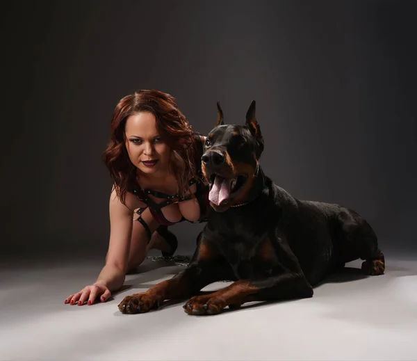 Sexy girl in black belts lying near dog in studio