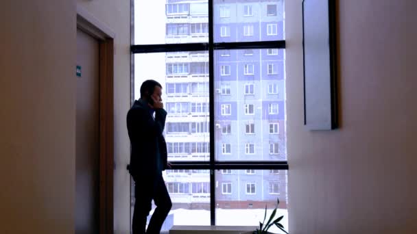 Мужчина разговаривает по телефону перед окном — стоковое видео