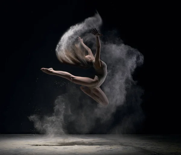 Girl in body jumps in dust cloud black background — Stock Photo, Image