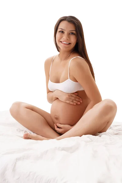 Pregnant woman posing in studio sitting on bed — Stock Photo, Image