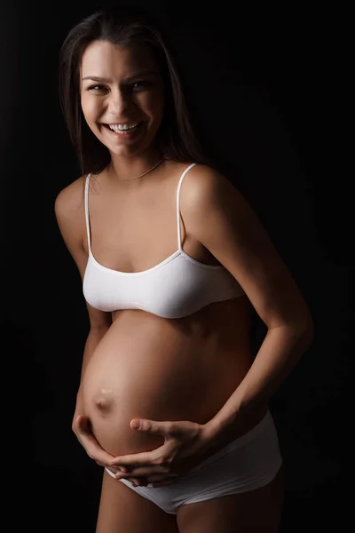 Těhotná mladá žena pózuje v prádlo s úsměvem — Stock fotografie