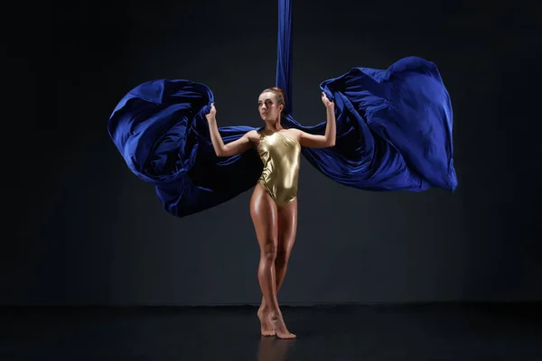 Slim girl in gold bodysuit on blue aerial silks — Stock Photo, Image