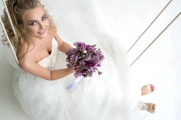 Jonge bruid in studio op schommel met mooie boeket — Stockfoto