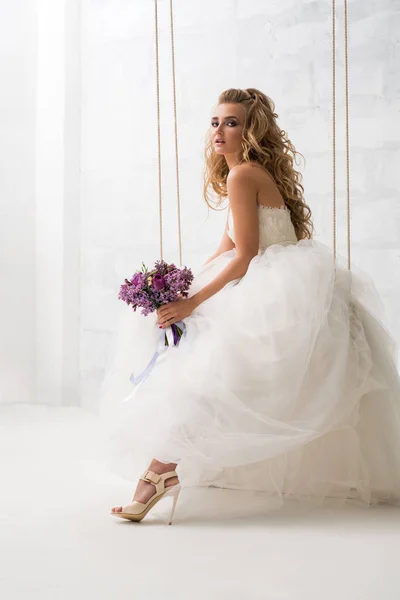 Belle mariée avec bouquet sur une balançoire en studio — Photo