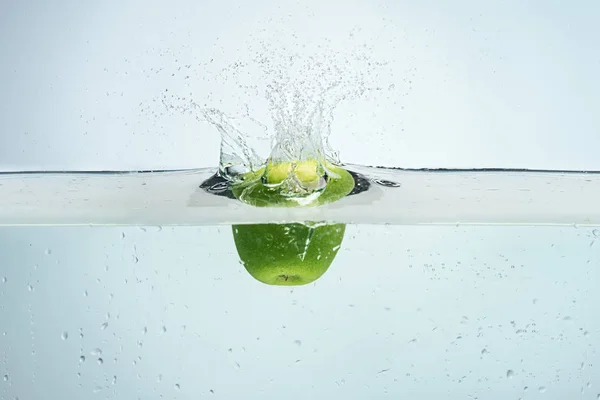 Single apple being dropped into blue water